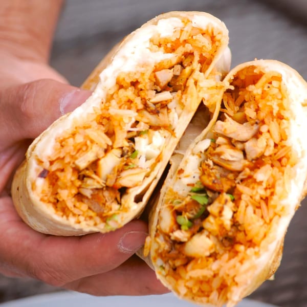 A person's hands holding a large burrito cut in half, revealing chicken, rice, and sauce.