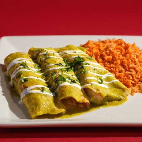 Three green enchiladas drizzled with white sauce and cilantro, served with orange rice on a white plate.